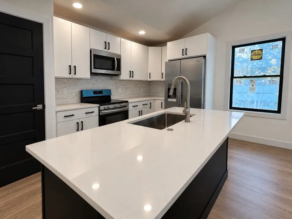Kitchen island with sink, white cabinets, stainless steel appliances and a window