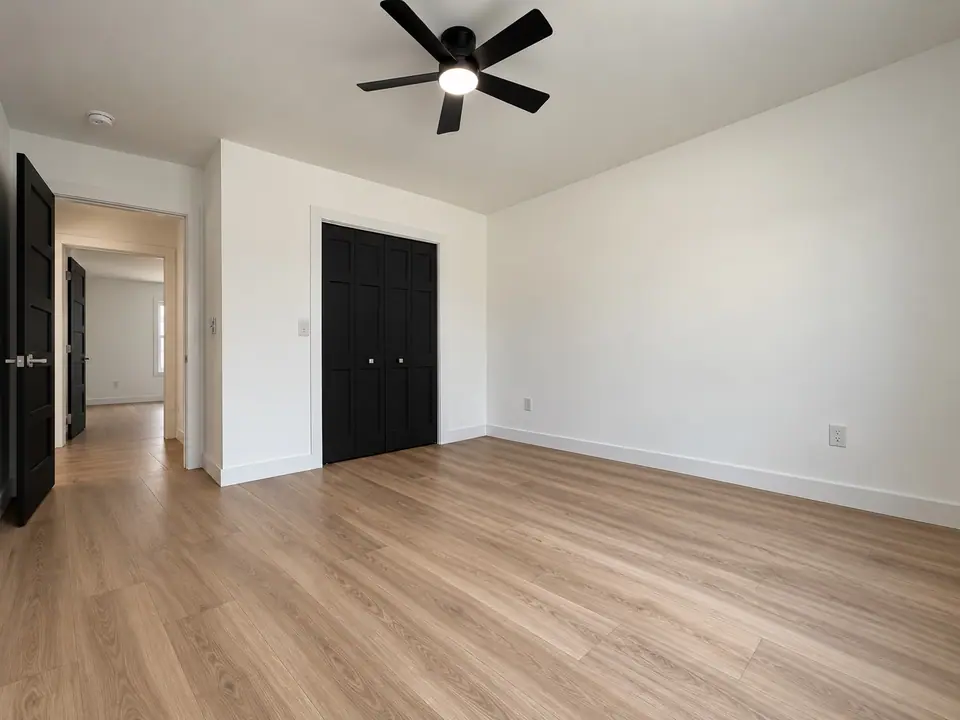 Bedroom with ceiling fan, black closet doors and an open doorway to the hall