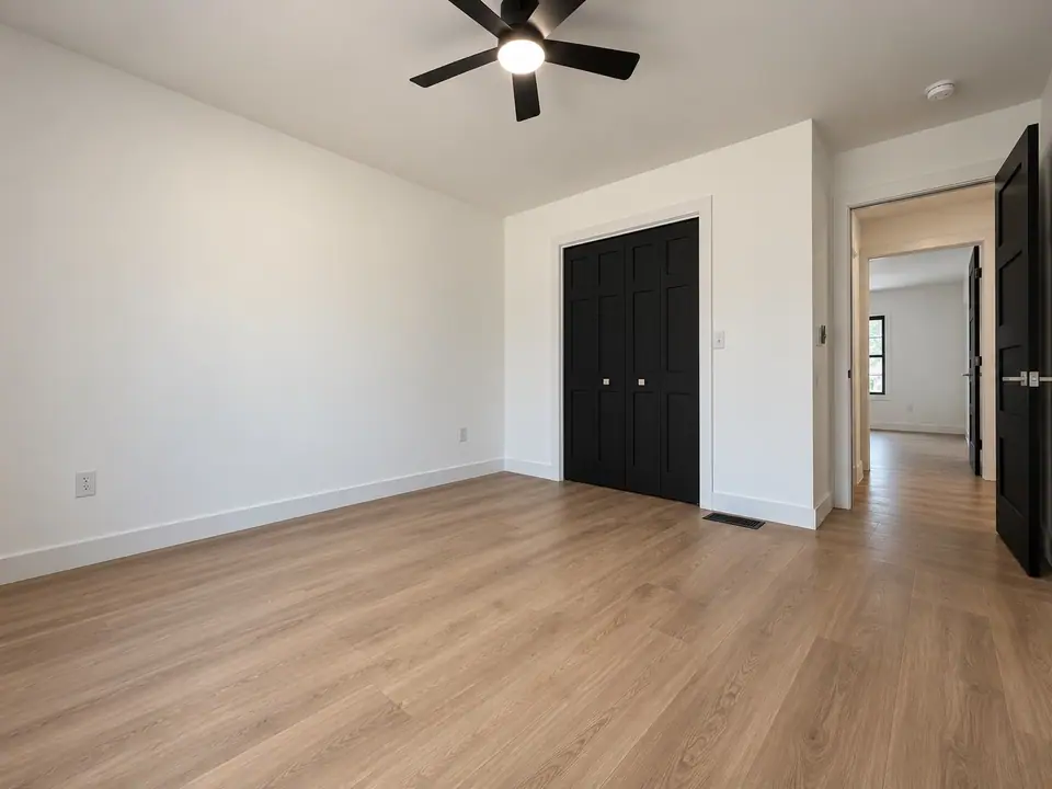 Bedroom with ceiling fan, black closet doors and a doorway to the hall